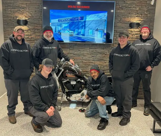The Car Doctor+ crew in shop hoodies, gathered in the lounge